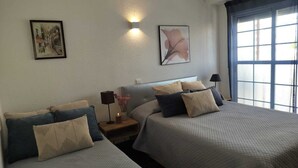 Habitación de hotel con dos camas, una mesita de noche con lámpara y obras de arte en las paredes.