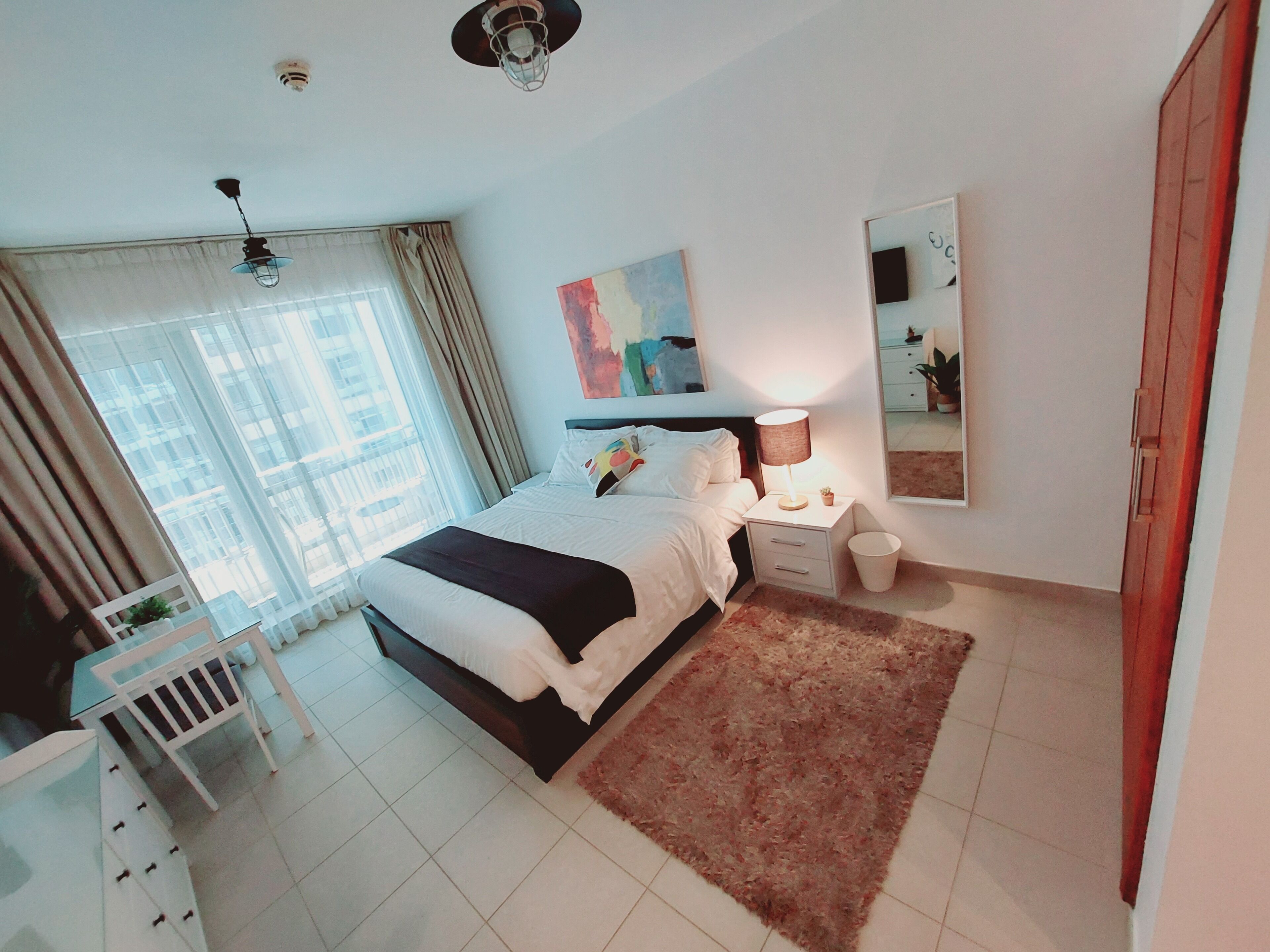 A modern bedroom with a large bed, bedside tables, a nightstand, a mirror, and a window with curtains.