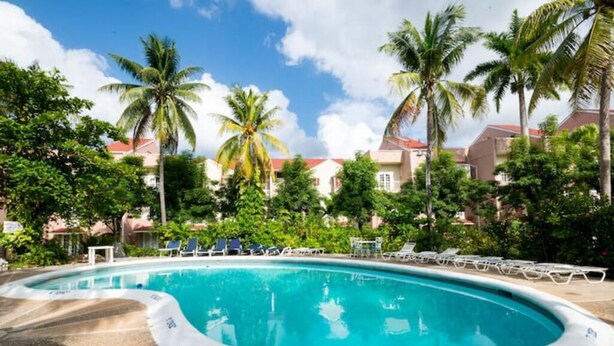 A swimming pool surrounded by palm trees and lounge chairs, with a clear sky above. - Ochi Beach Getaway (Unknown)