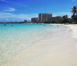 A beach with clear turquoise water, a sandy shore, and a hotel in the background. - Ochi Beach Getaway (Unknown)