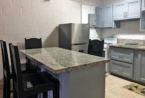 A compact kitchen with a granite countertop, a stainless steel refrigerator, and light blue cabinets. - Ochi Beach Getaway (Unknown)