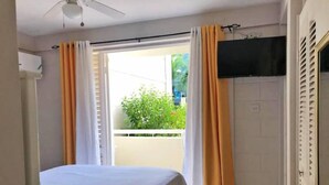 A bedroom with a bed, a ceiling fan, a TV mounted on the wall, and a window with curtains. - Ochi Beach Getaway (Unknown)