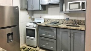 A compact kitchen with grey cabinets, a stainless steel refrigerator, a white stove, and a microwave. - Ochi Beach Getaway (Unknown)