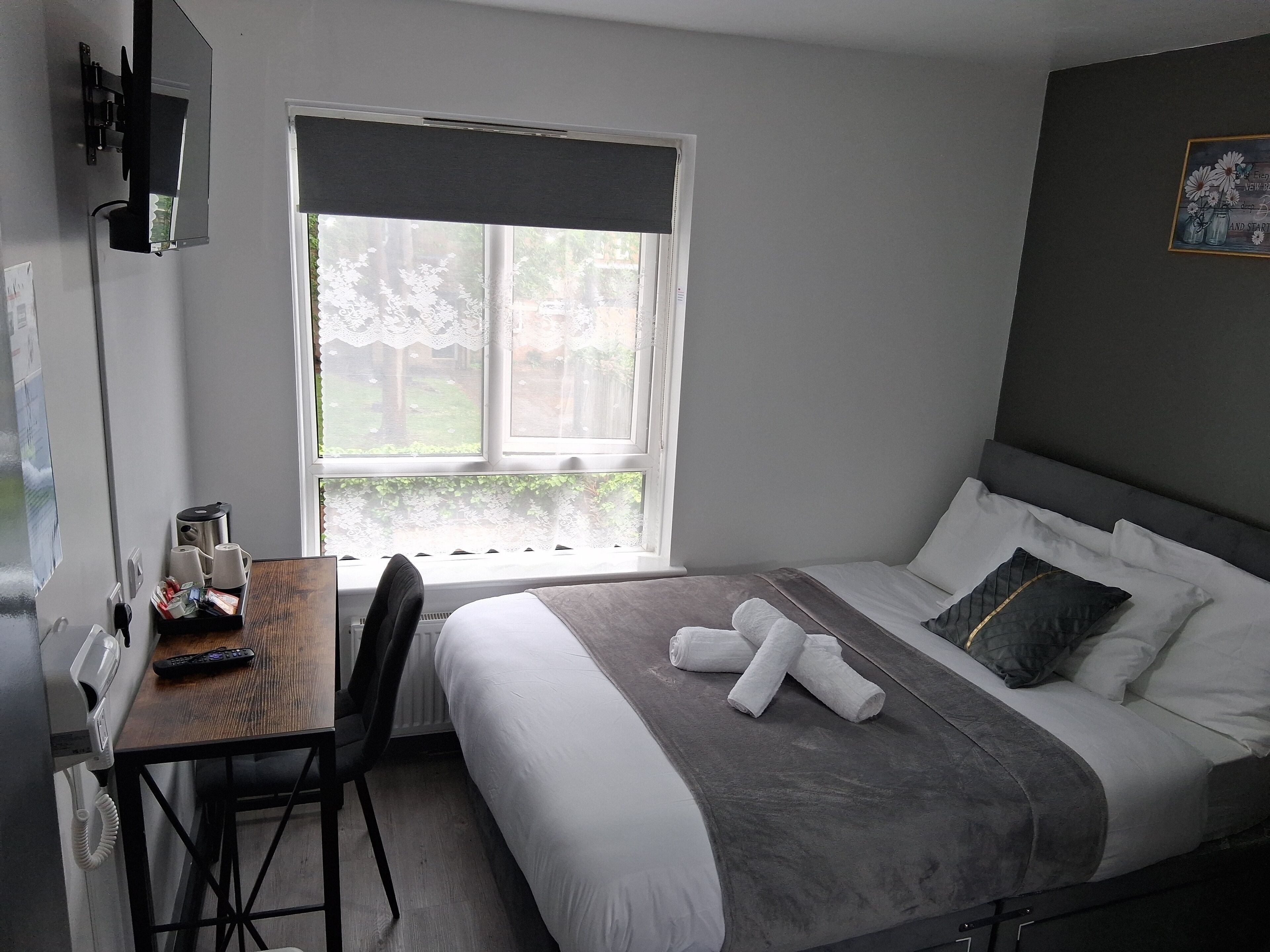 Een hotelkamer met een bed, een bureau met telefoon, een stoel en een raam met uitzicht op groen.