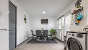 A compact kitchen with a built-in washing machine, a dining area with two chairs, and a flat-screen TV mounted on the wall. - Premium Serviced Accommodation Nottingham - 4 Bedrooms - All Ensuite - Sleeps 7 (Nottingham)