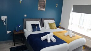 A hotel room with a bed, a bedside table with a lamp, a wall-mounted hairdryer, and a poster. - Premium Serviced Accommodation Nottingham - 4 Bedrooms - All Ensuite - Sleeps 7 (Nottingham)