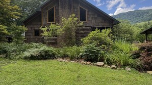A rustic stone house with a chimney, surrounded by lush greenery and a clear blue sky. - River falls cabin sleeps 6 (Marietta)