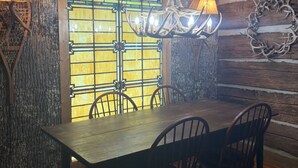 A rustic dining area with a wooden table and chairs, a stained glass window, and a chandelier with antlers. - River falls cabin sleeps 6 (Marietta)