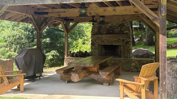 A covered outdoor area with a stone fireplace, wooden benches, and a large table. - River falls cabin sleeps 6 (Marietta)
