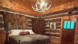 A log cabin bedroom with a bed, a chandelier, a wooden door, and a rug. - River falls cabin sleeps 6 (Marietta)