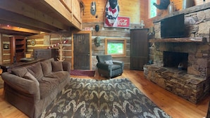 A rustic interior with a stone fireplace, wooden beams, a leather sofa, and a cozy fireplace area. - River falls cabin sleeps 6 (Marietta)