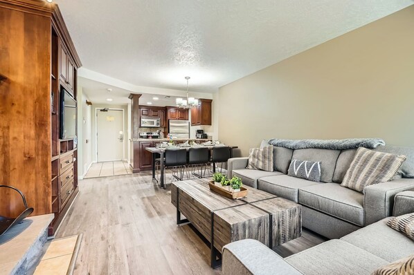 A modern kitchen with dark wood cabinets, a central island, and a dining area with a gray sofa and coffee table.