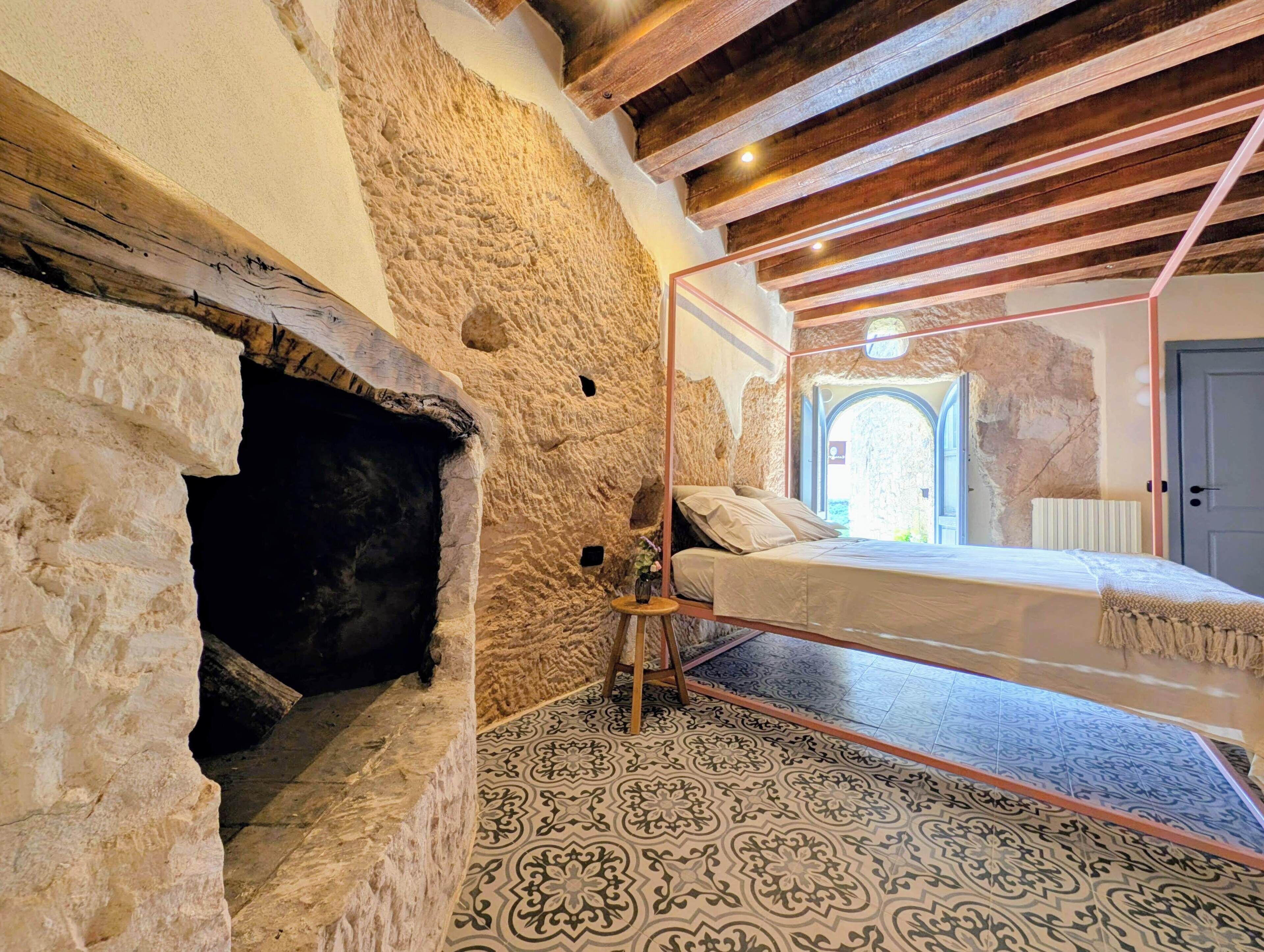 A rustic room with exposed stone walls, a bed with a glass enclosure, and a patterned floor.