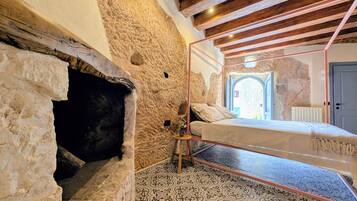 A rustic room with exposed stone walls, a bed with a glass enclosure, and a patterned floor.