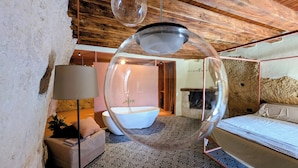 Un dormitorio con una cama grande, una lámpara colgante esférica y una bañera al fondo.