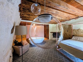 Un dormitorio con una cama grande, una lámpara colgante esférica y una bañera al fondo.