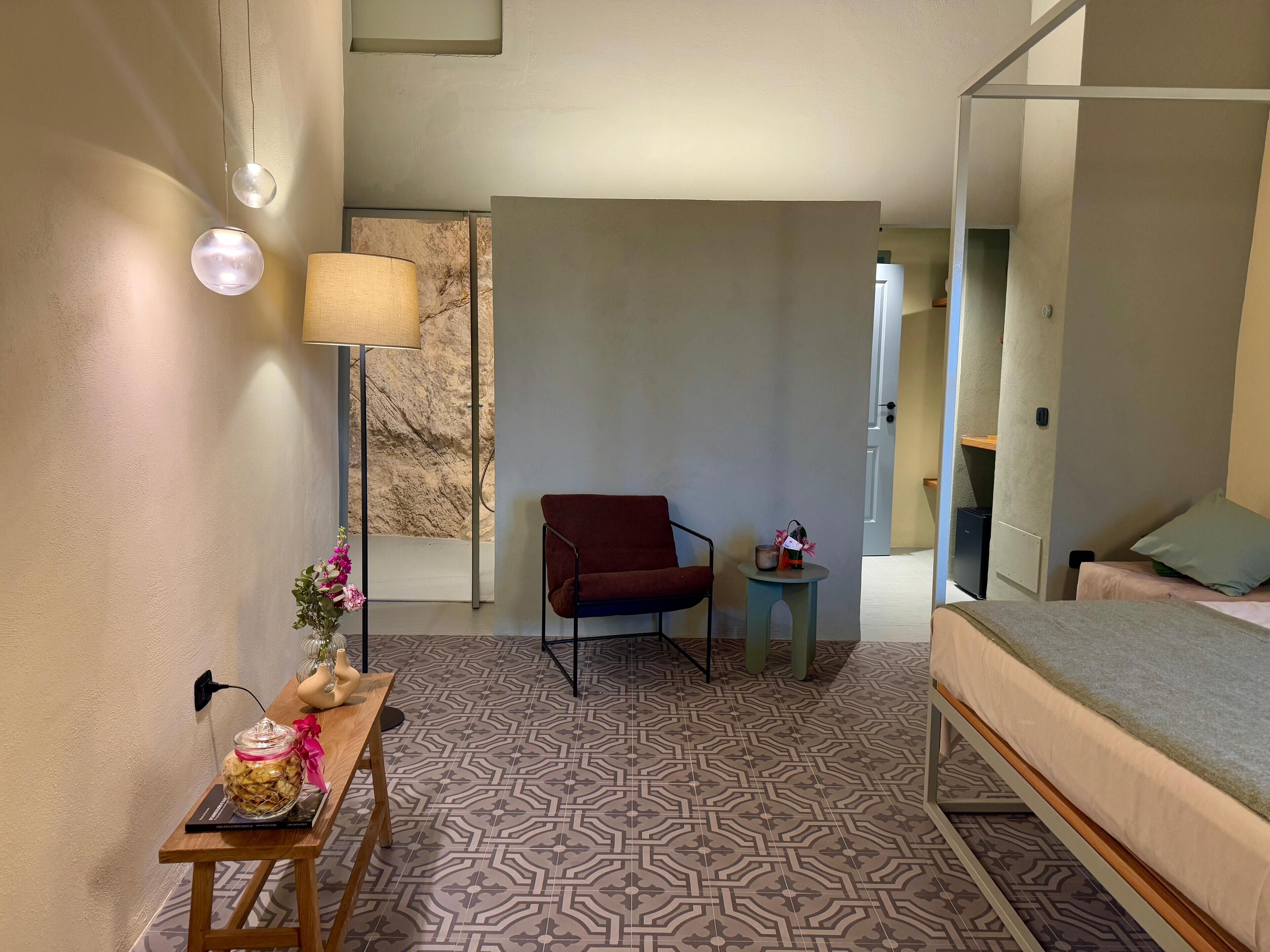 Una camera d'hotel moderna con pavimento a motivi, un letto, una poltrona rossa, un piccolo tavolo con una lampada e un vaso decorativo.