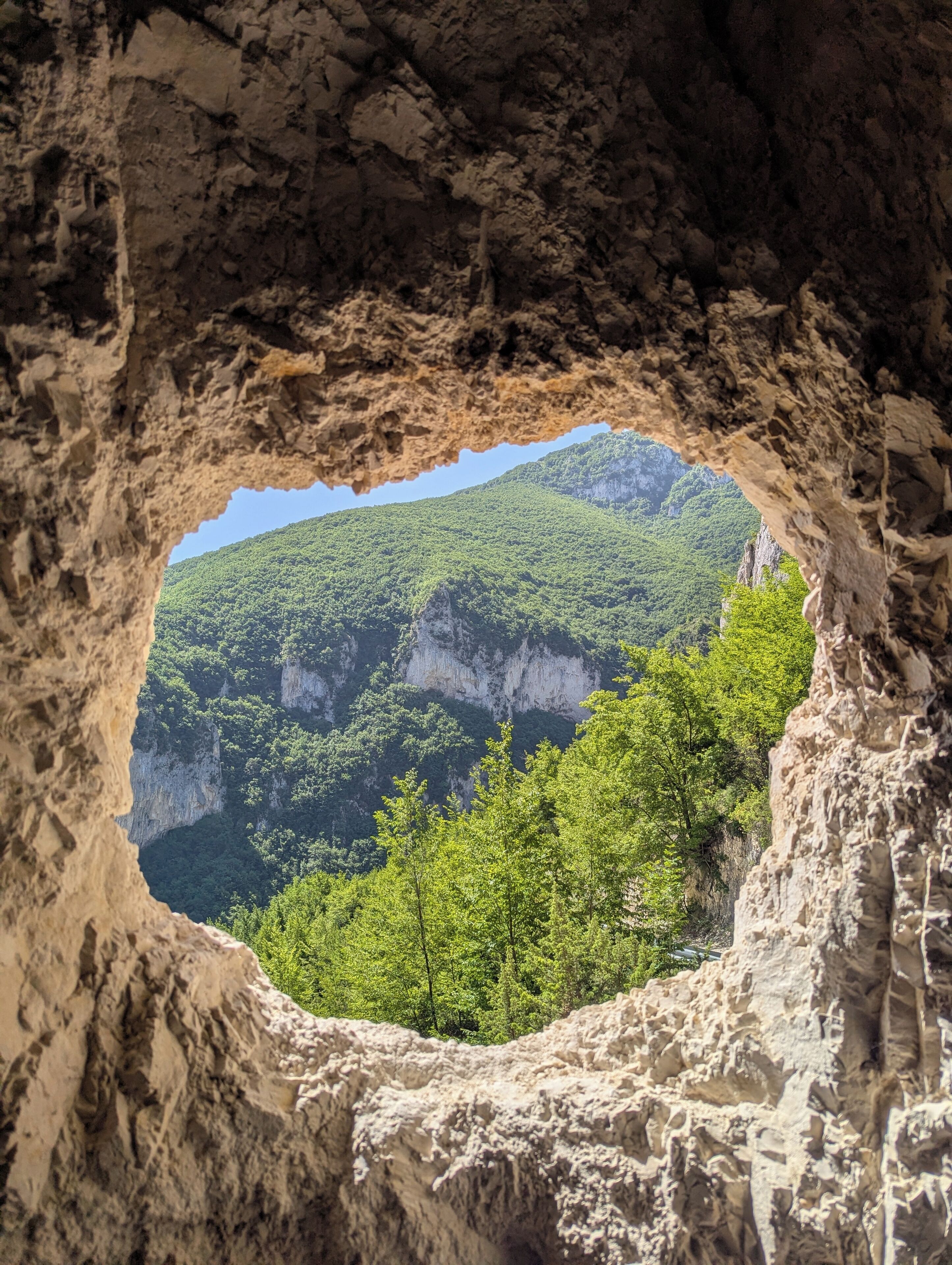 Abertura natural de caverna com vista para um vale arborizado.