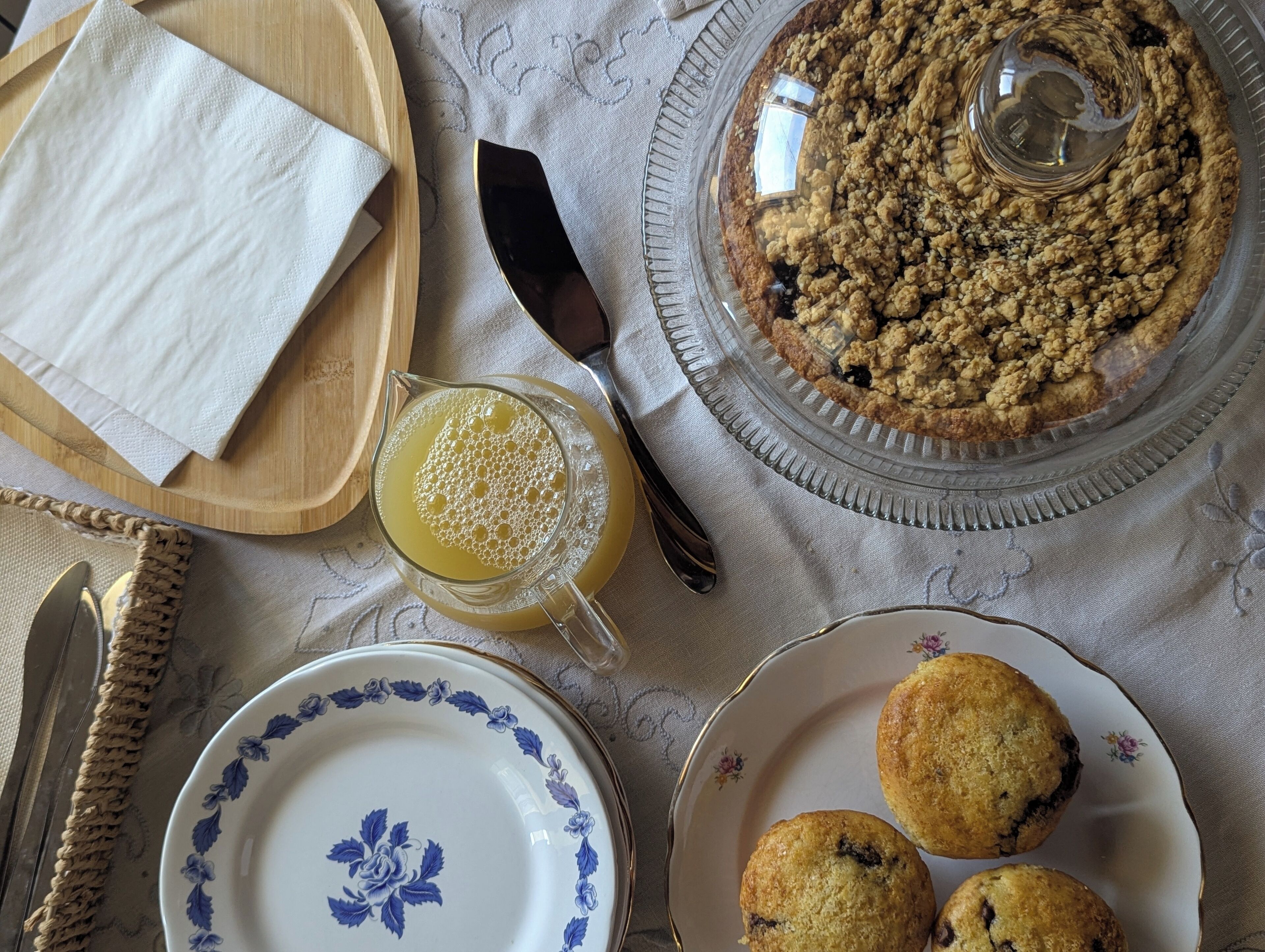 Une table avec une tarte, des muffins, un pichet de jus de fruits et une assiette décorée de motifs floraux.