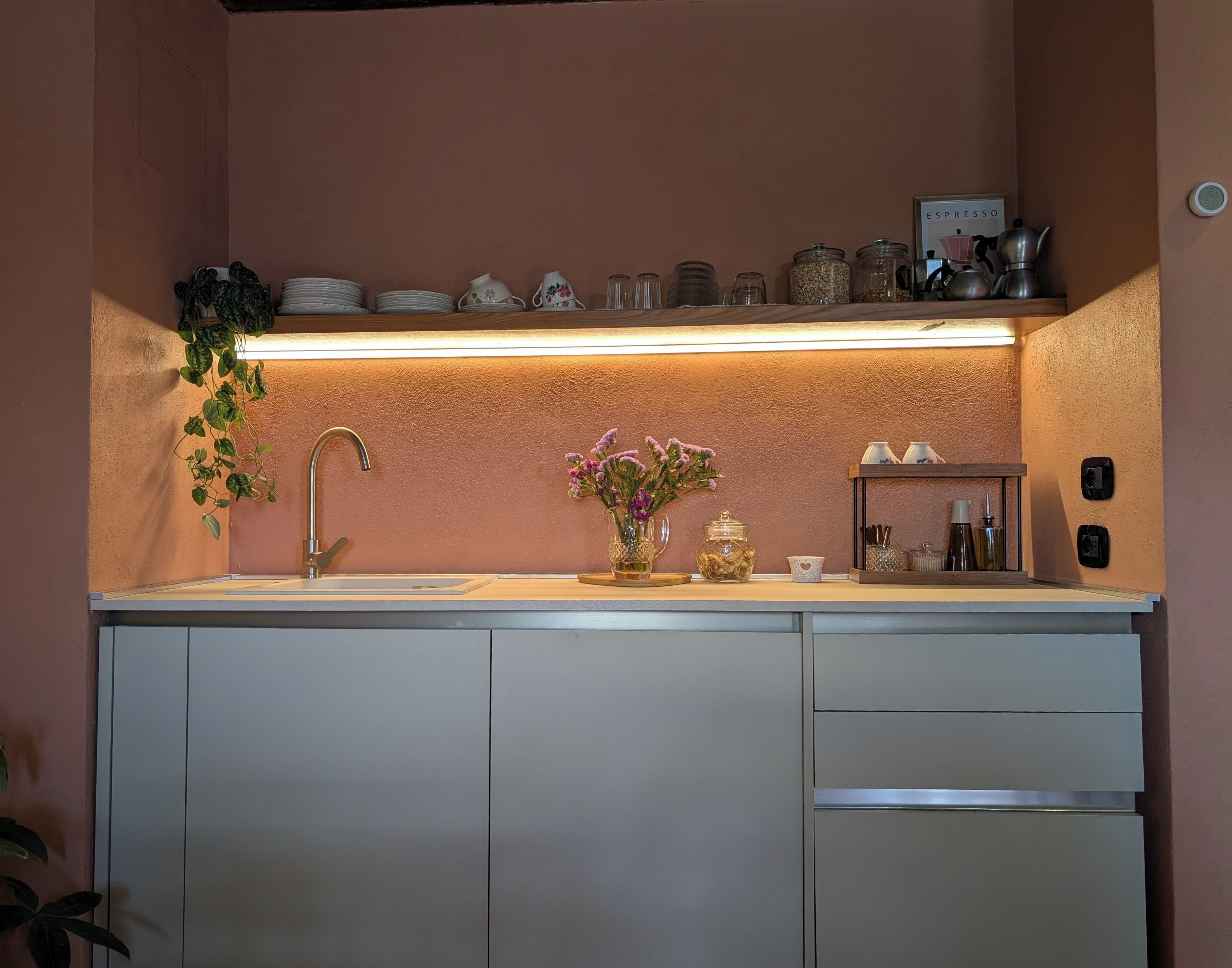 A kitchen with a built-in sink, a countertop with various jars and a coffee maker, and a wall-mounted shelf above the sink.