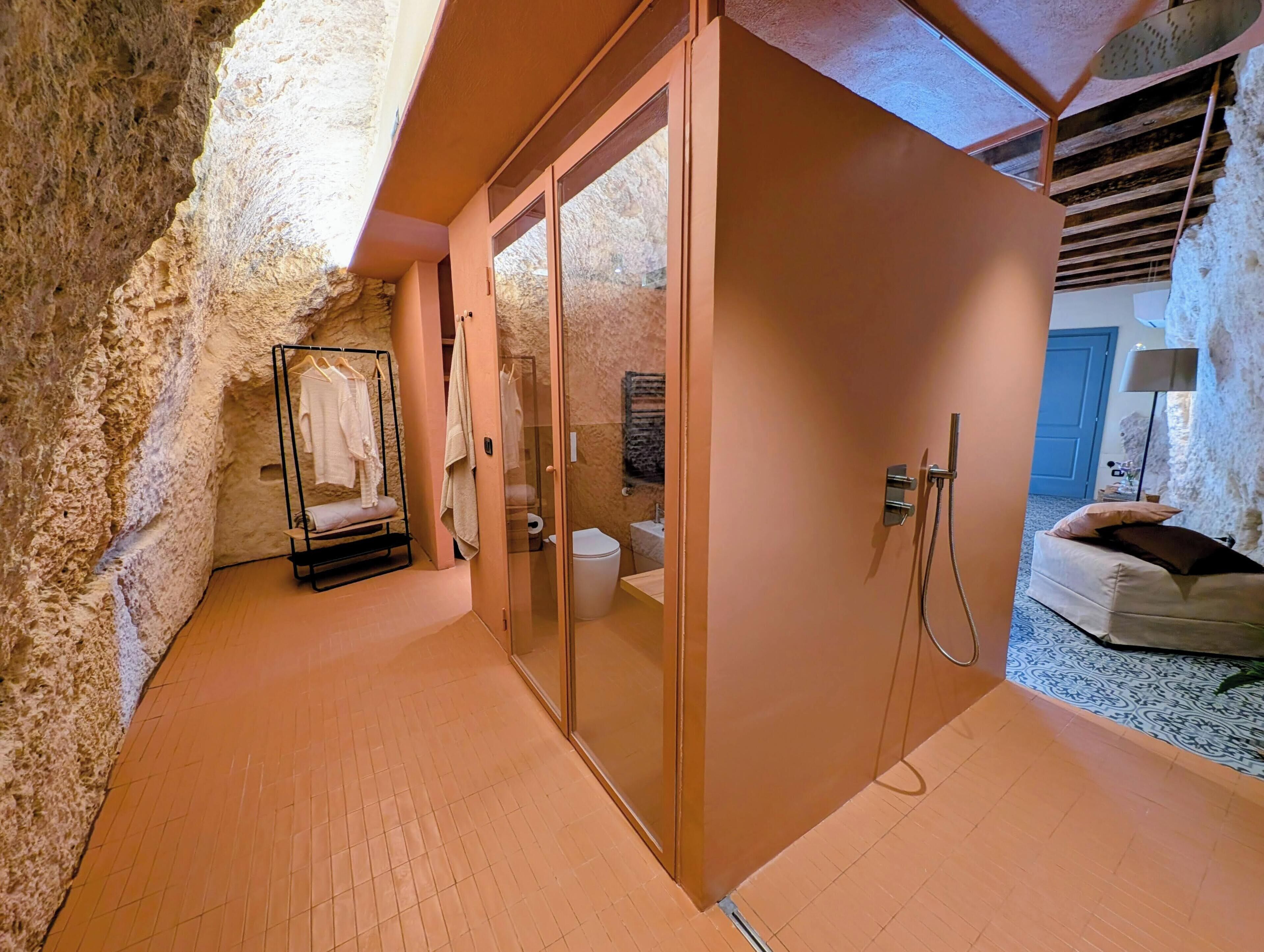 A bathroom with a stone wall, a glass shower enclosure, and a wooden floor.