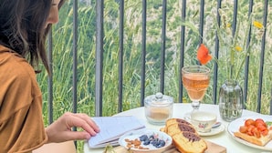 Una persona sentada a una mesa con comida y documentos, con vistas a un paisaje montañoso.