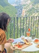 Una persona sentada a una mesa con comida y documentos, con vistas a un paisaje montañoso.