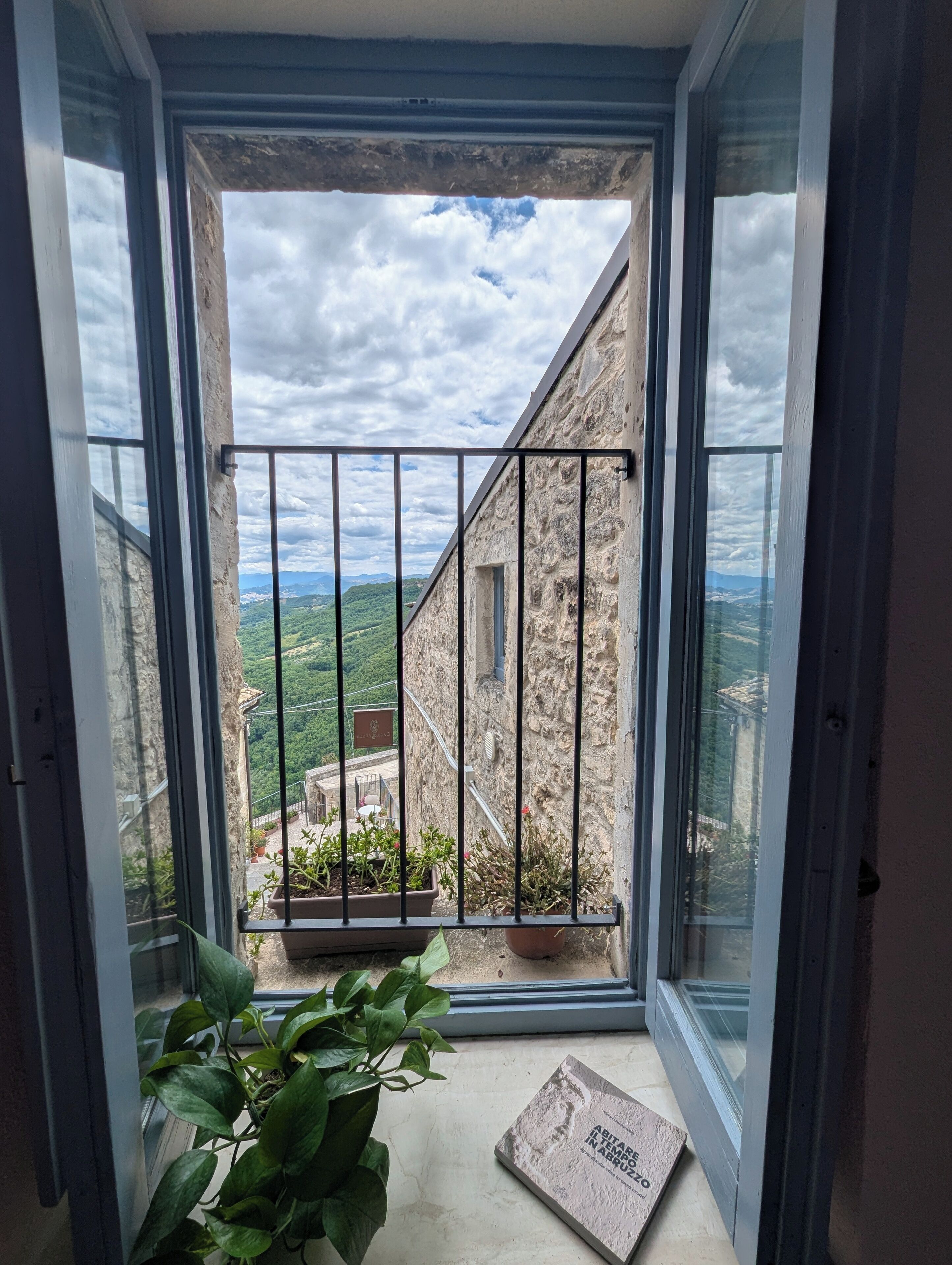 A balcony with a stone wall, a metal railing, and a view of a green landscape.