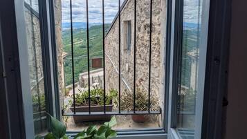 A balcony with a stone wall, a metal railing, and a view of a green landscape.