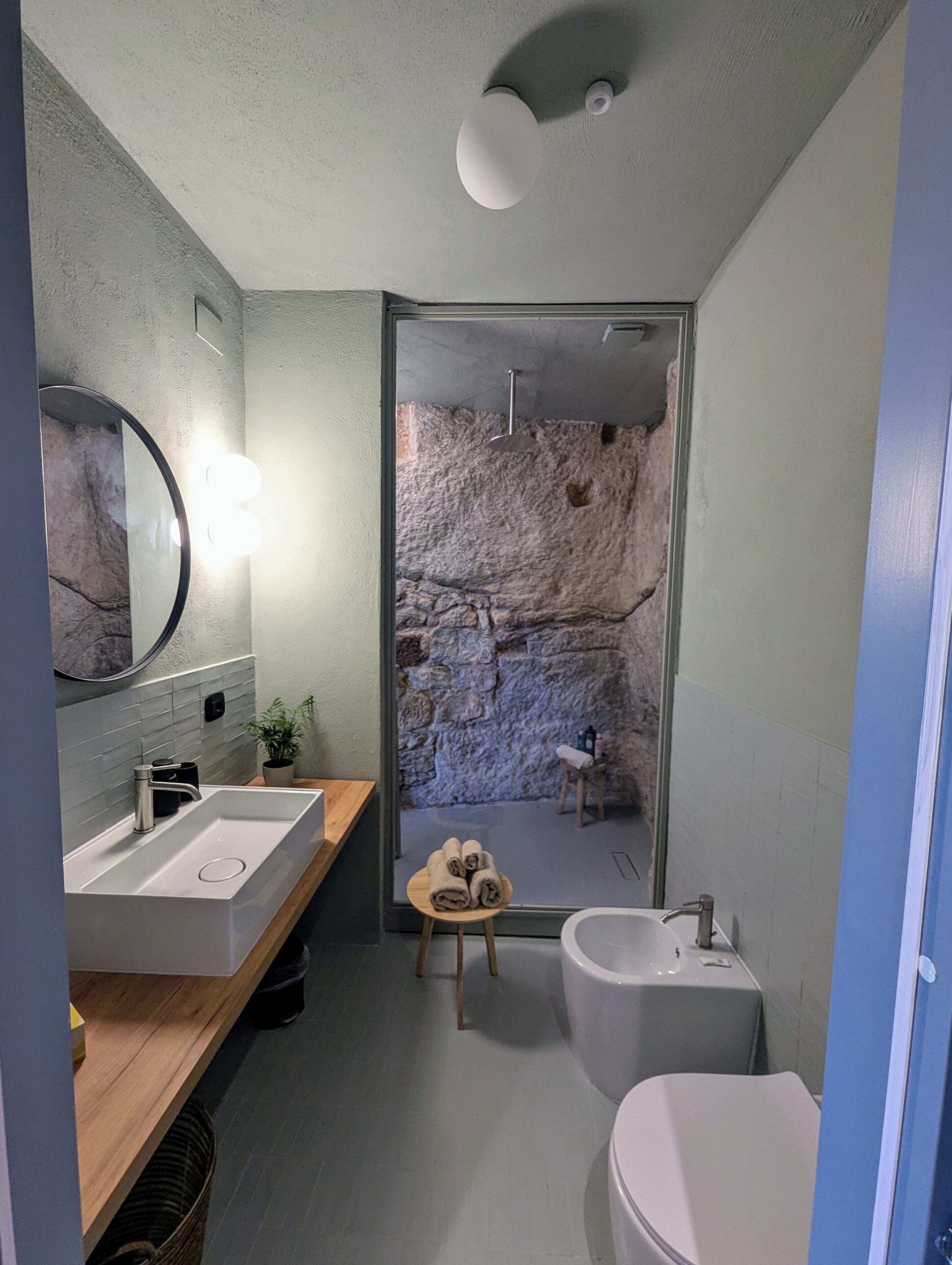 Un baño moderno con pared de piedra, tocador de madera, espejo redondo y inodoro blanco.