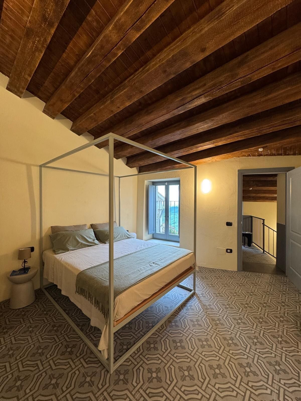 Ein Schlafzimmer mit einem Himmelbett, einem Fenster mit Blick und einem Musterparkett.