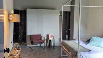 Une chambre avec un lit à baldaquin, une petite table avec une lampe, une chaise et un objet décoratif posé sur une table d’appoint.