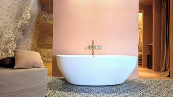 Ein modernes Badezimmer mit einer freistehenden Badewanne, einem beigefarbenen Sofa, gemusterten Bodenfliesen und einer strukturierten Wand.