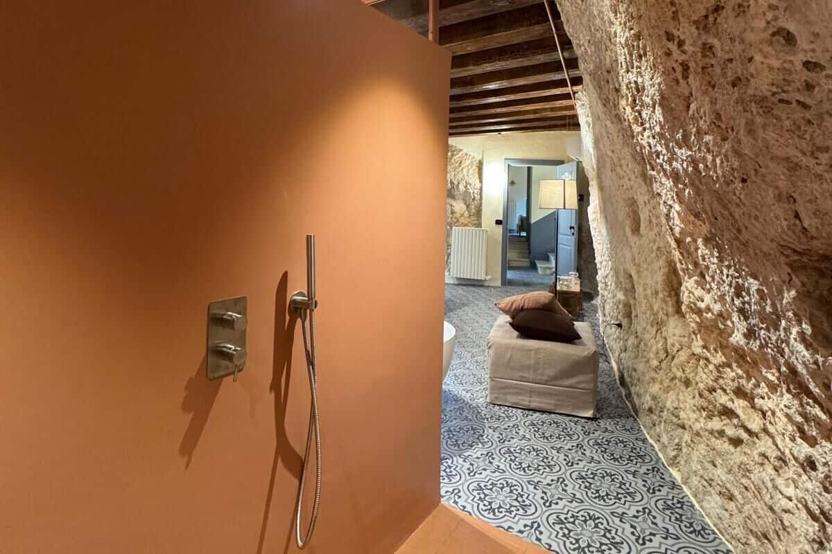 A modern bathroom with a shower, a patterned floor, and a stone wall.