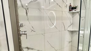 Ein modernes Badezimmer mit Marmorwänden, einer Duschkabine aus Glas und einem Duschboden mit Kieselsteinen.