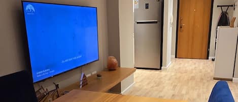 Un saló modern amb una taula baixa de fusta, un sofà blau, un televisió de pantalla plana, un refrigerador i una porta de fusta.