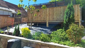 A wooden deck with a pergola, surrounded by various plants and a small tree.