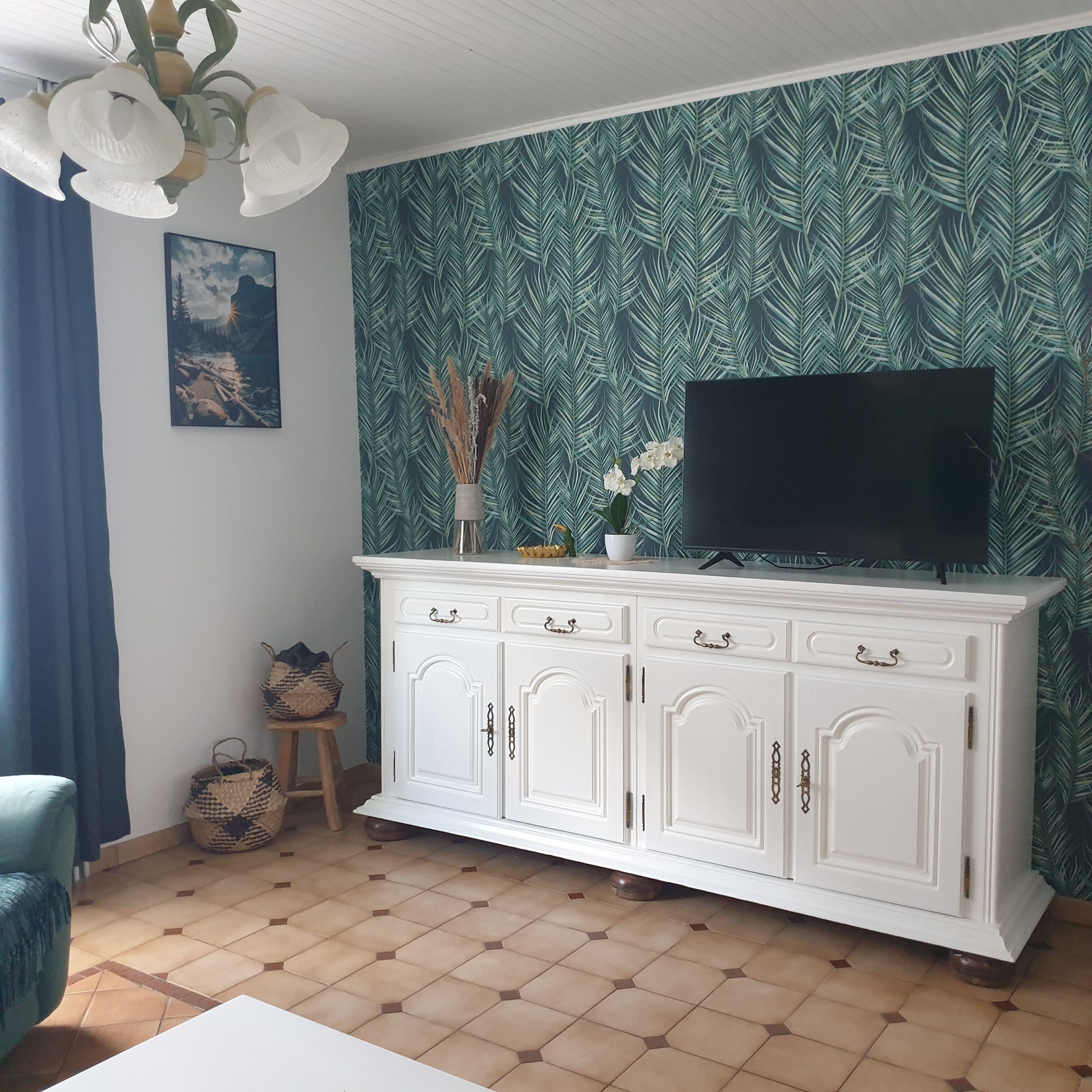 Un salon avec un meuble blanc, un téléviseur à écran plat posé sur le dessus, un mur à motifs et un tableau accroché au mur.