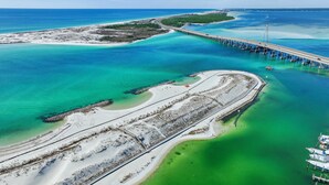 An aerial view of a coastal area with a bridge, clear turquoise waters, and a sandy beach. - Seaside Solace (Destin)