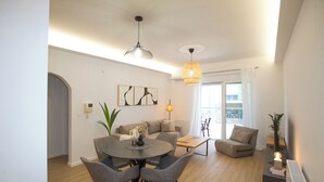 A modern living room with a dining table, grey chairs, a sofa, and a coffee table. There is a plant, a lamp, and artwork on the wall. - K11 Apartment in Athens Downtown (Athina)
