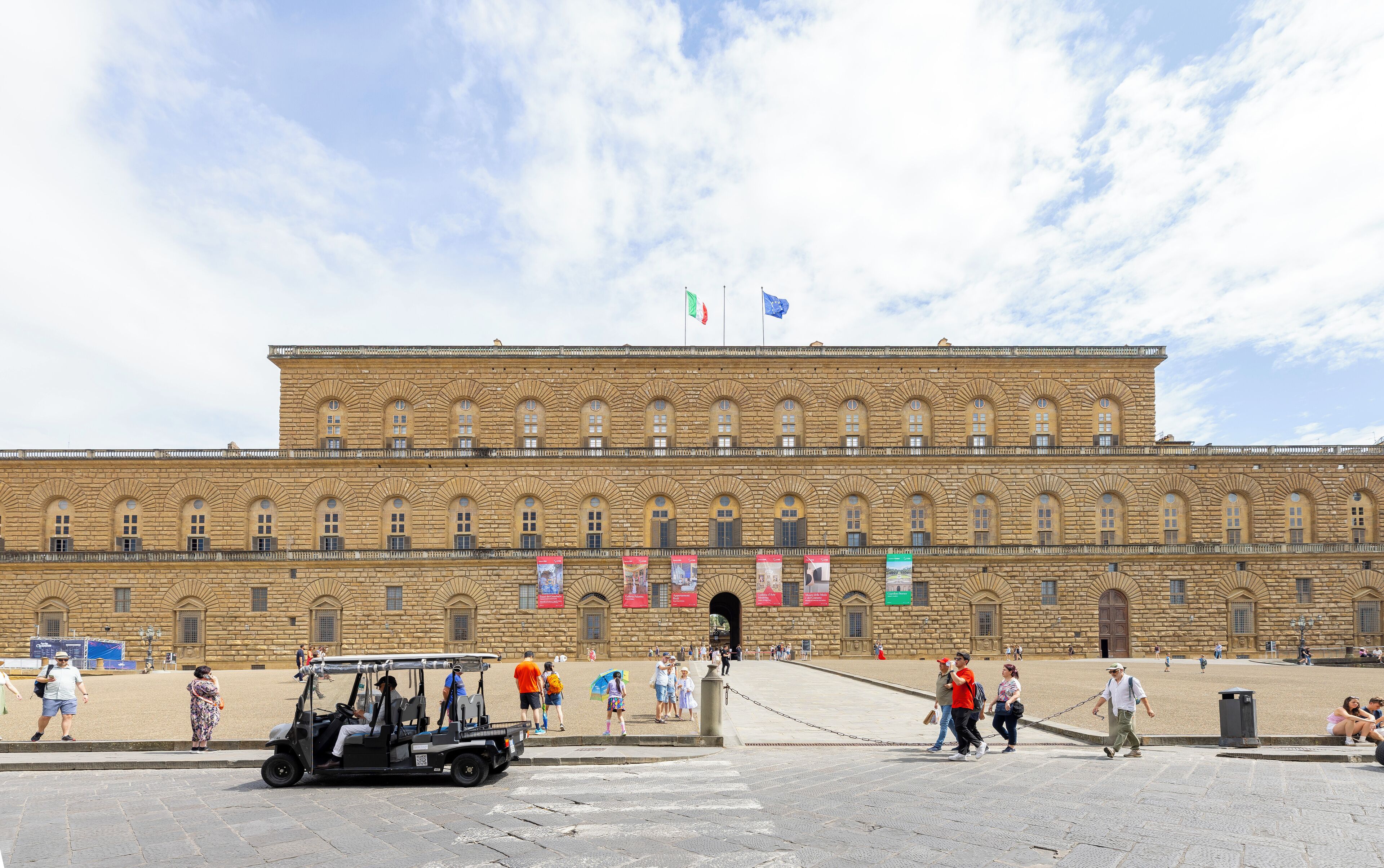 A large historic building with a symmetrical facade, multiple arched windows, and flags on top.