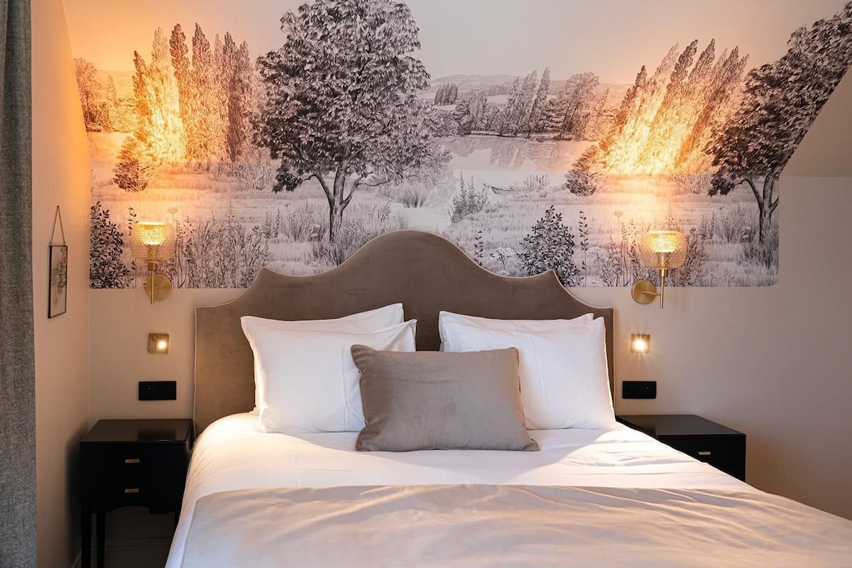 A bedroom with a bed, two bedside tables, and a wall-mounted lamp.