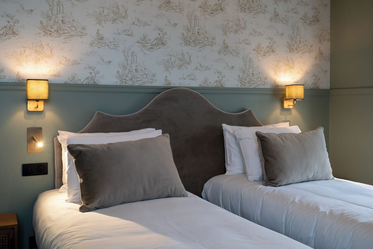 A double bed with a headboard, two wall-mounted lamps, and a patterned wallpaper.