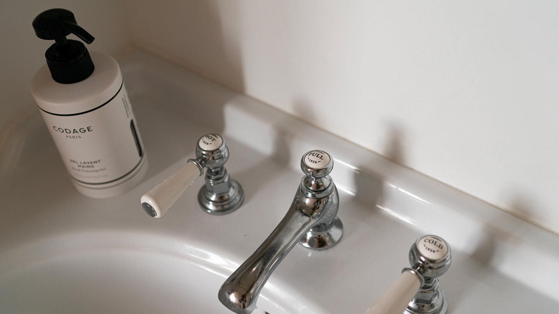 A bathroom sink with a bottle of Codage Paris hair product and a faucet with temperature control knobs.