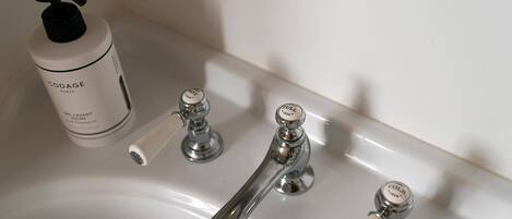 A bathroom sink with a bottle of Codage Paris hair product and a faucet with temperature control knobs.