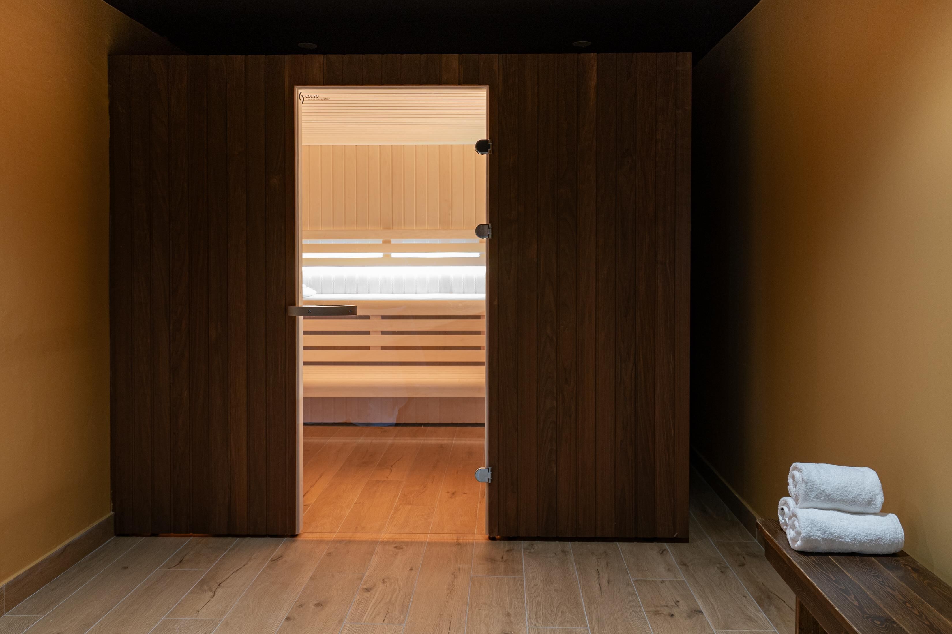 Una habitación con un armario de madera, una cama con ropa de cama blanca y un par de toallas sobre un banco.