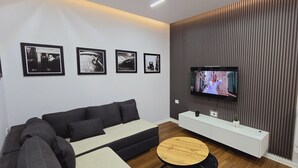 Ein modernes Wohnzimmer mit einer Couch, einem an der Wand montierten Fernseher und einem weißen Konsolentisch.