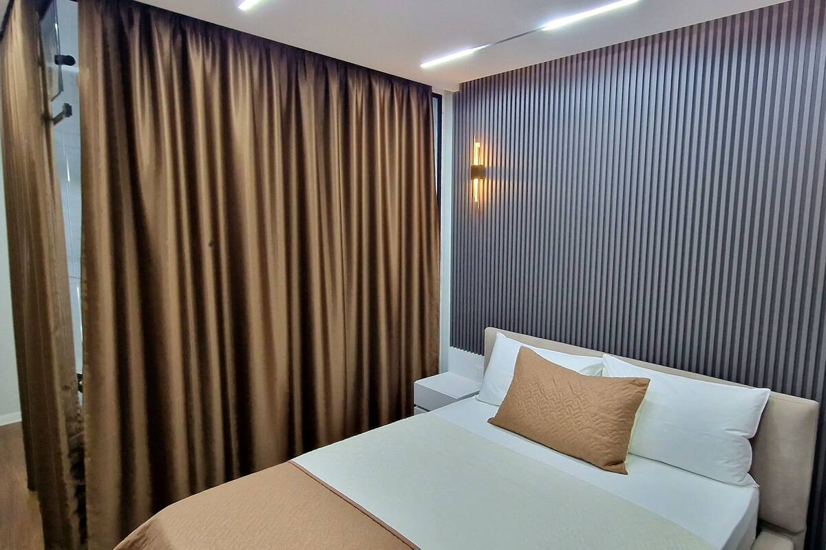 A hotel room with a bed, a nightstand, a wall-mounted light, and a curtain.