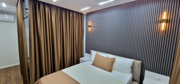 Una camera d'albergo con un letto, un comodino, una lampada a parete e una tenda.
