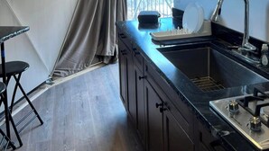 A modern kitchen with a black countertop, stainless steel sink, and a gas stove. There is a window with curtains and a round mirror on the wall.